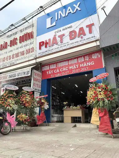 Cửa vào của một cửa hàng Inax với các băng rôn quảng cáo và hoa trang trí.